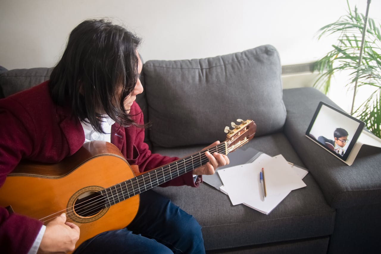 Man with long hair playing acoustic guitar during an online lesson at home.